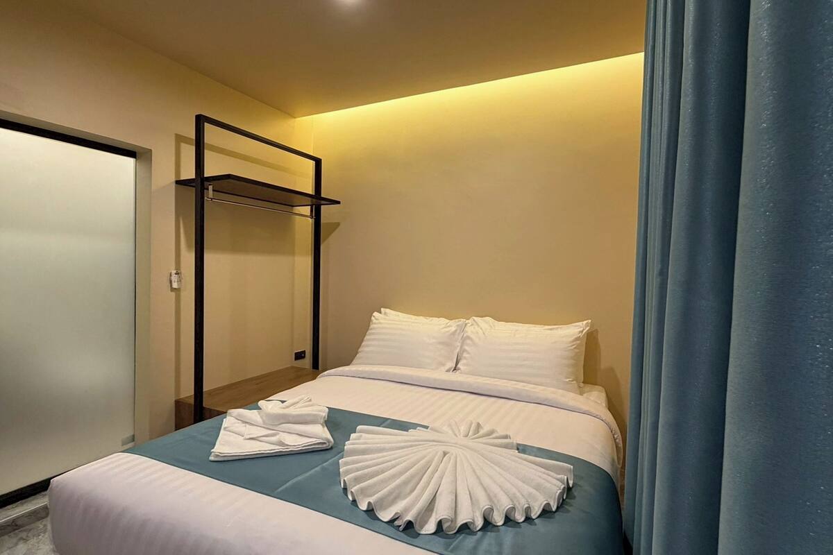 Un lit bien fait, avec du linge de lit blanc et un élément décoratif bleu, un porte-serviettes et une porte fermée.