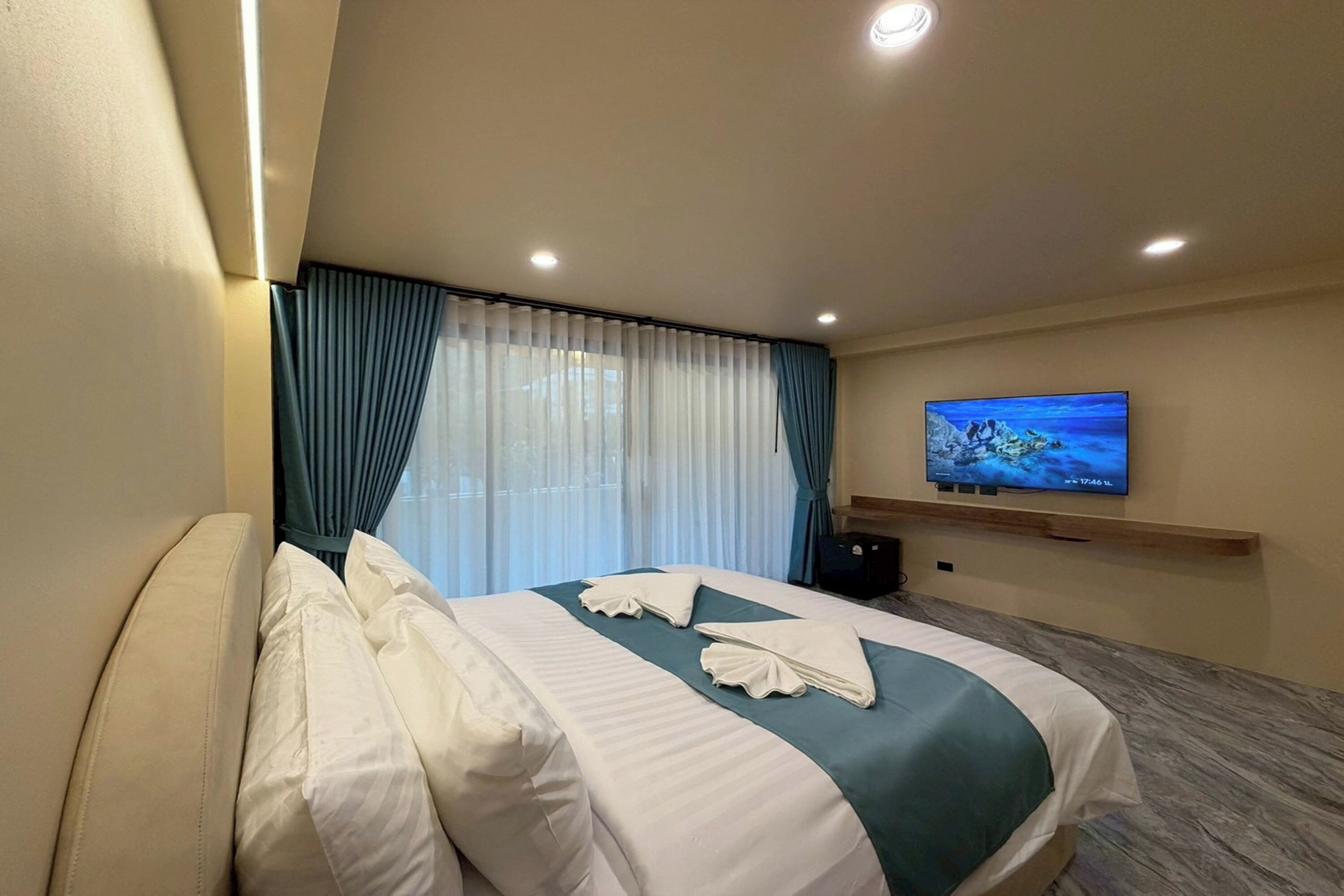 Habitación de hotel con cama, televisión en la pared y ventana con cortinas.