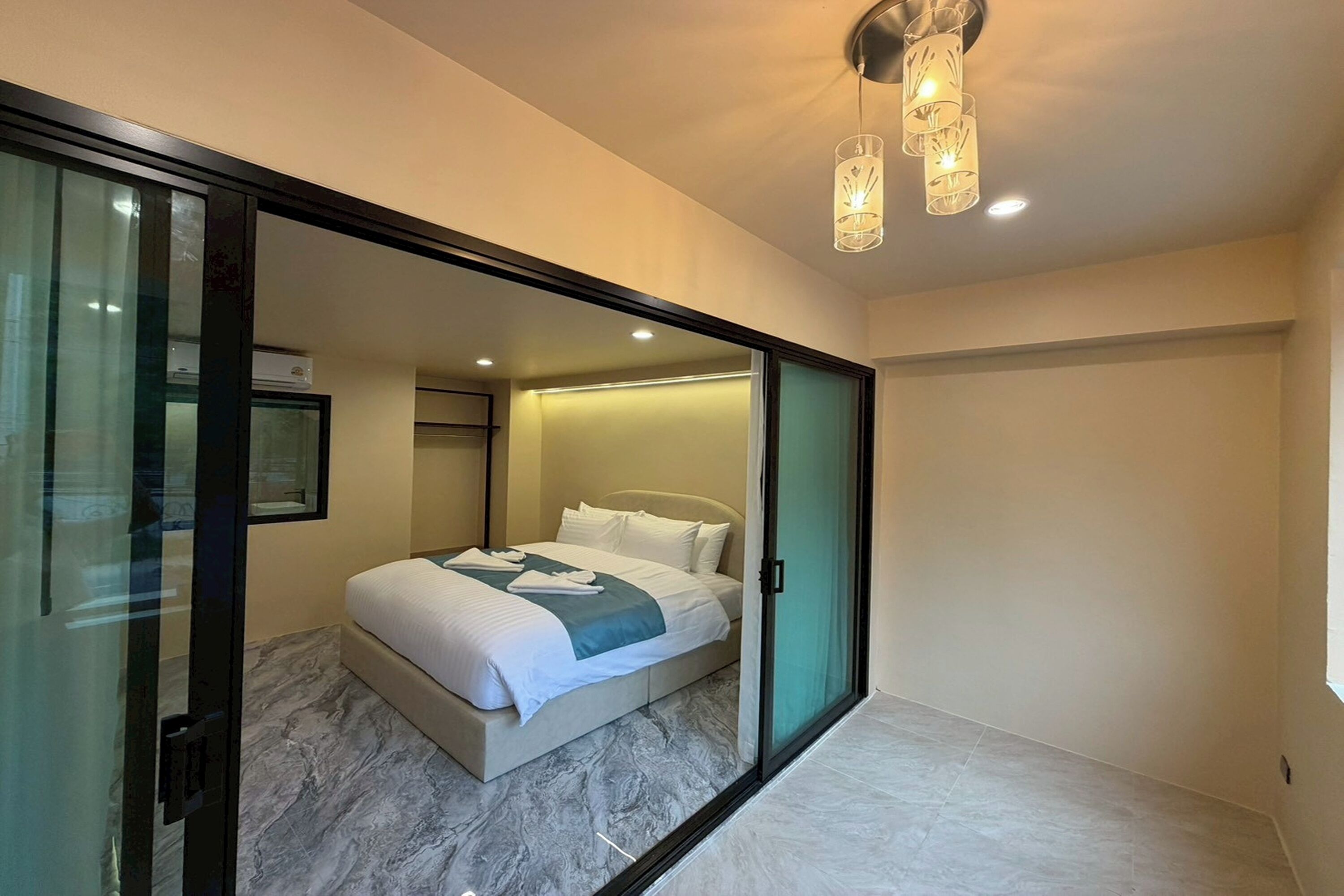 A modern hotel room with a bed, a glass partition, and a ceiling light fixture.