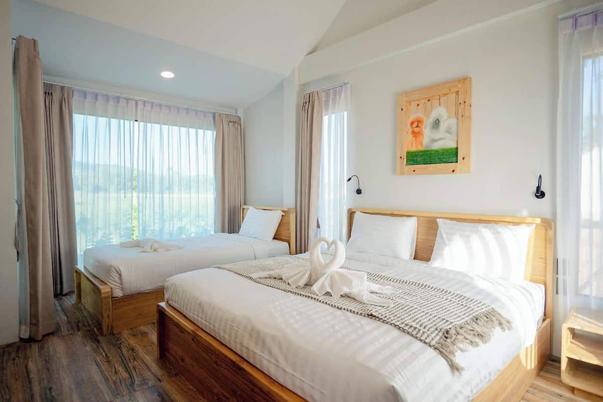 Habitación de hotel con dos camas, cabeceros de madera, ropa de cama blanca, un cuadro en la pared y vistas a través de amplias ventanas.