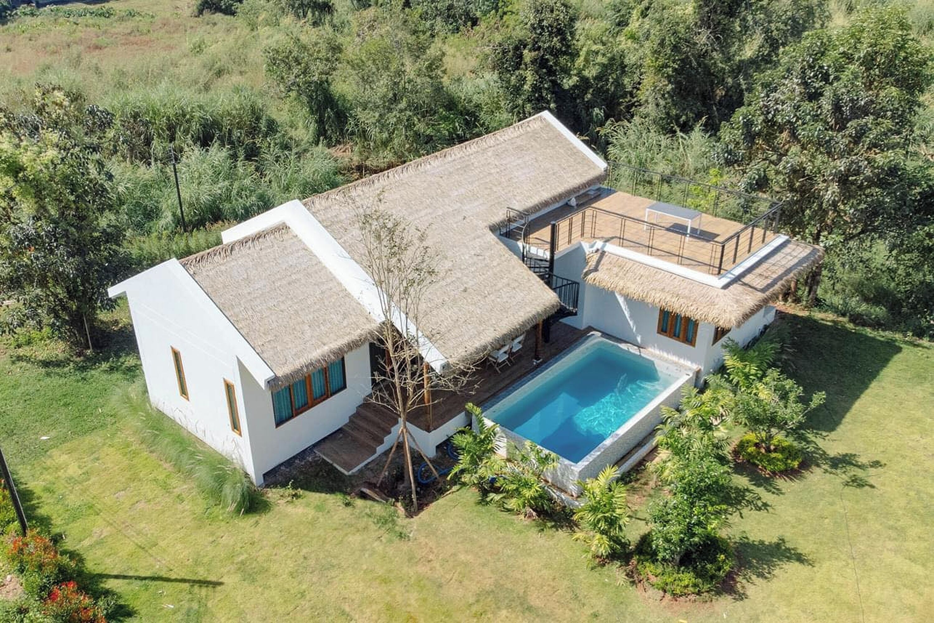 Une maison à deux étages avec un toit de chaume, une piscine et un jardin.