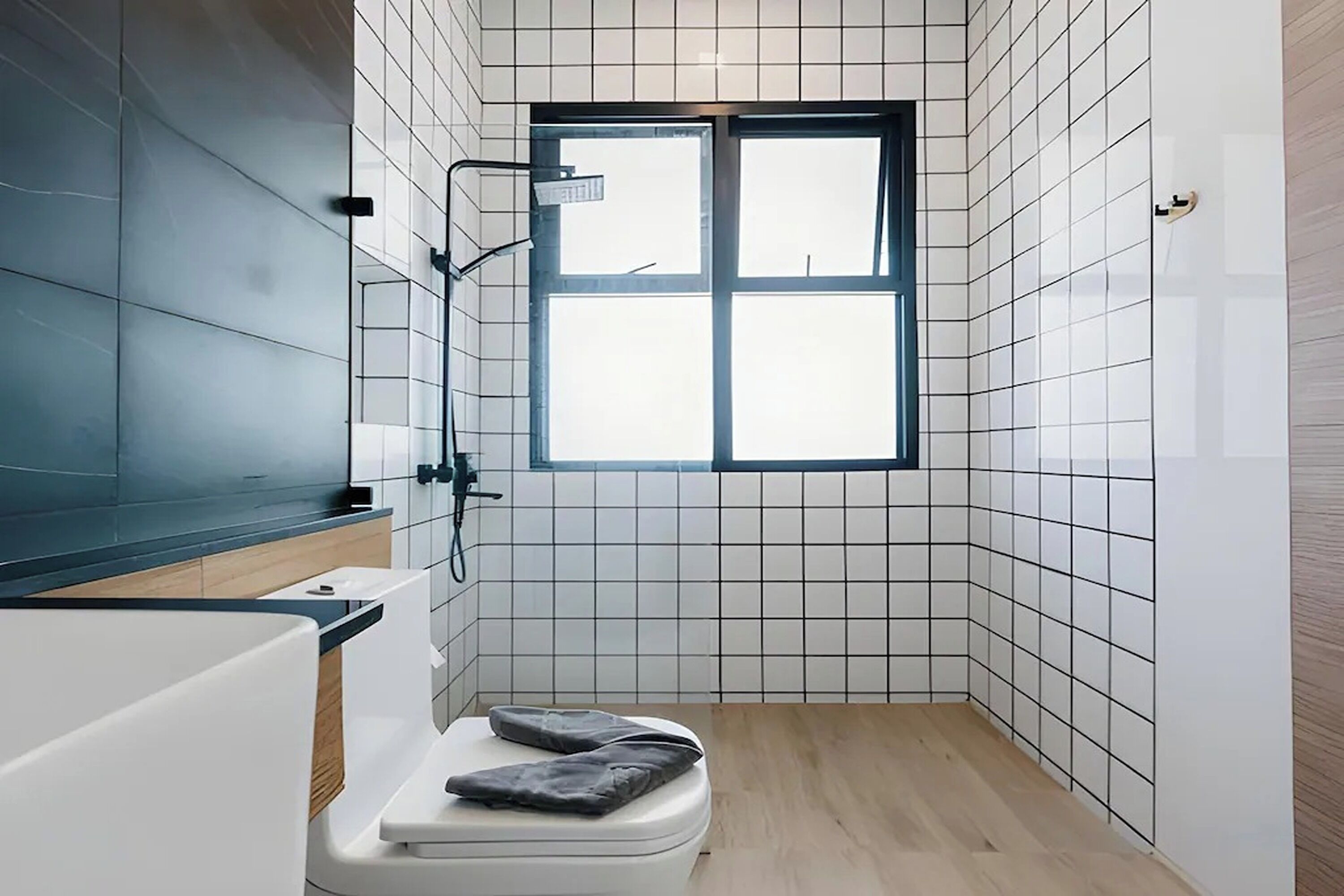 A bathroom with white tiled walls, a wooden floor, a white toilet, and a window with a view.