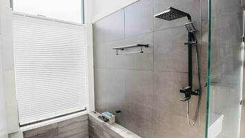 Un bagno moderno con box doccia in vetro, portasci asciugamani e una finestra con persiane.