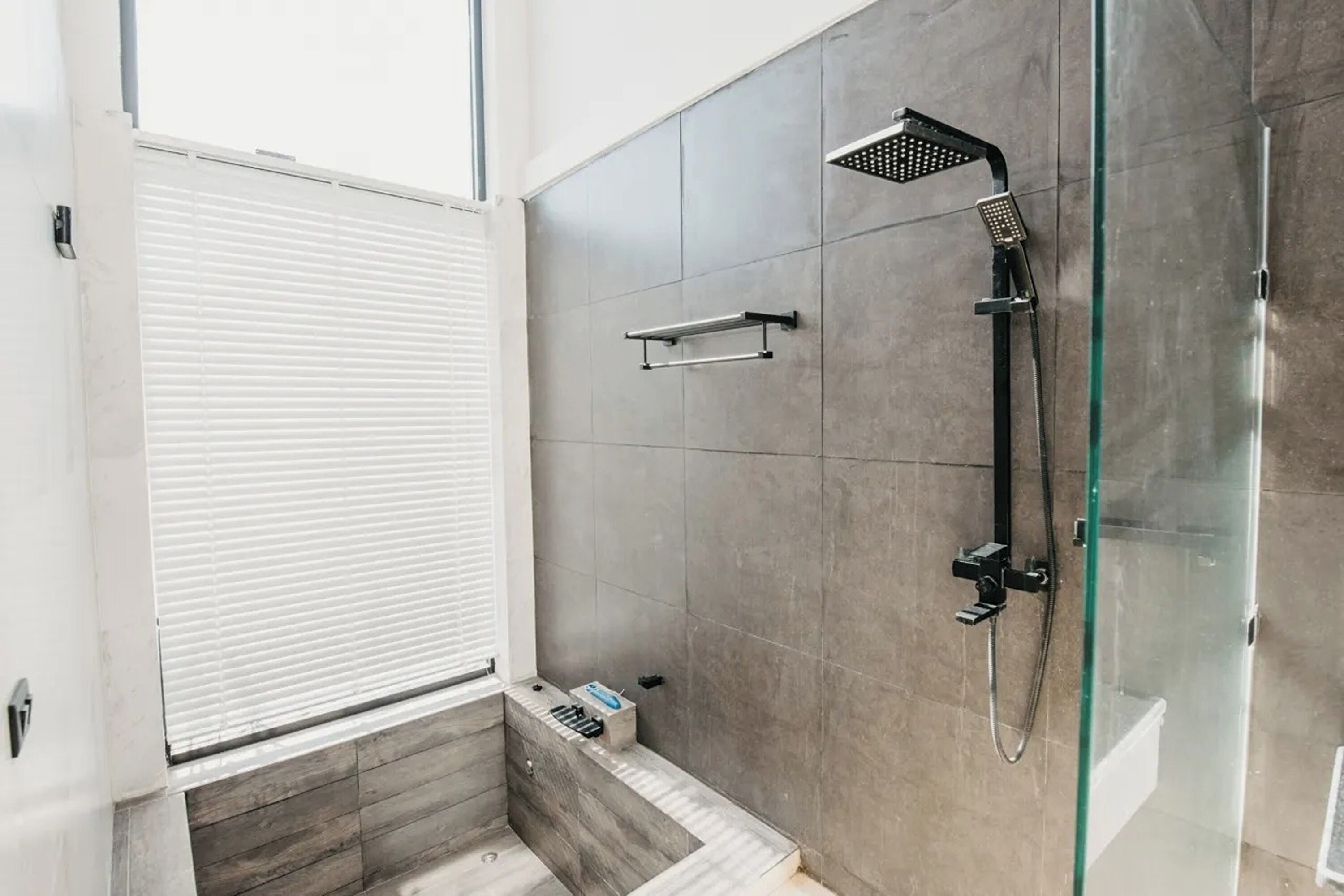 A modern bathroom with a glass shower enclosure, a towel rack, and a window with blinds.