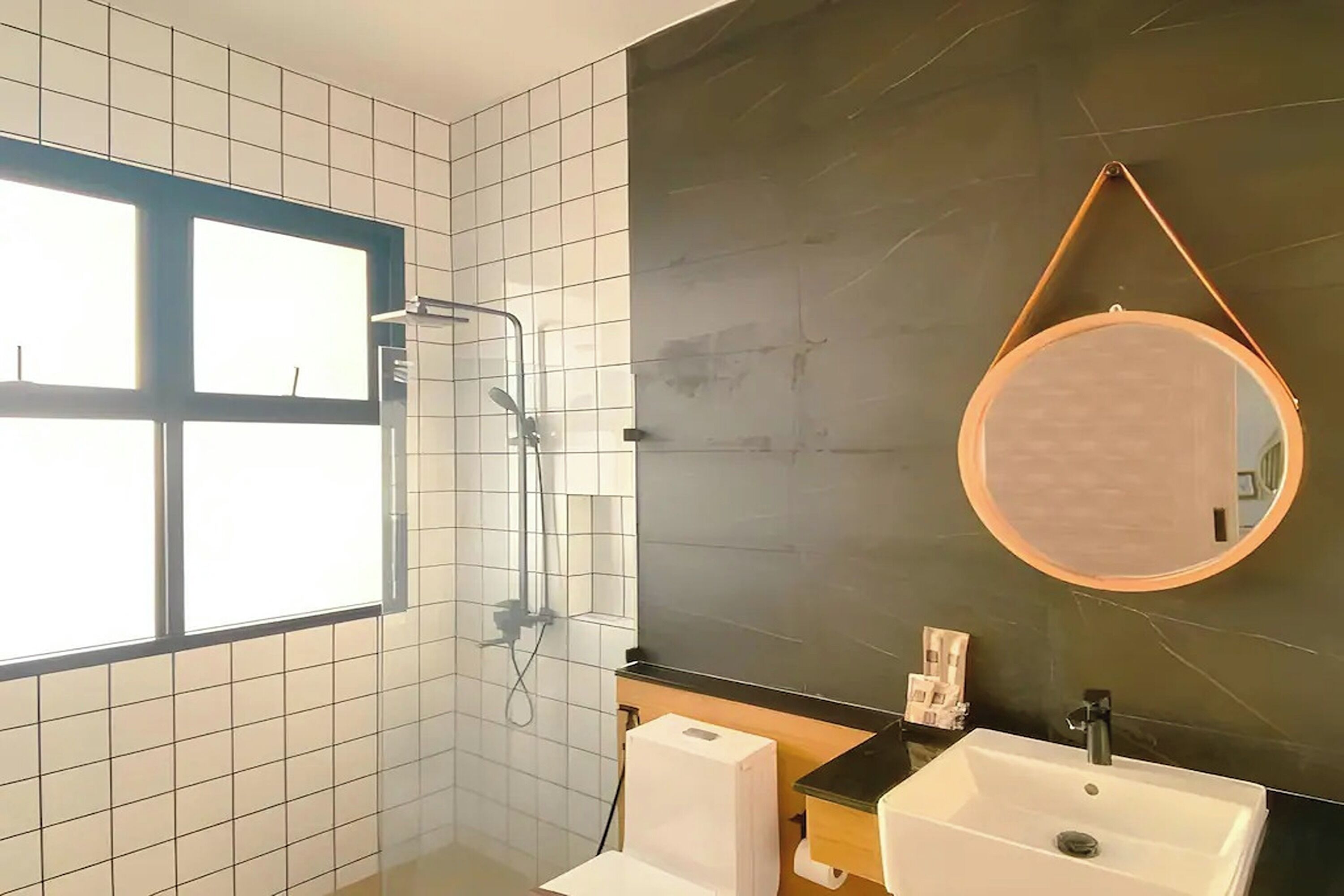 A bathroom with a shower, a sink, a mirror, and a window.