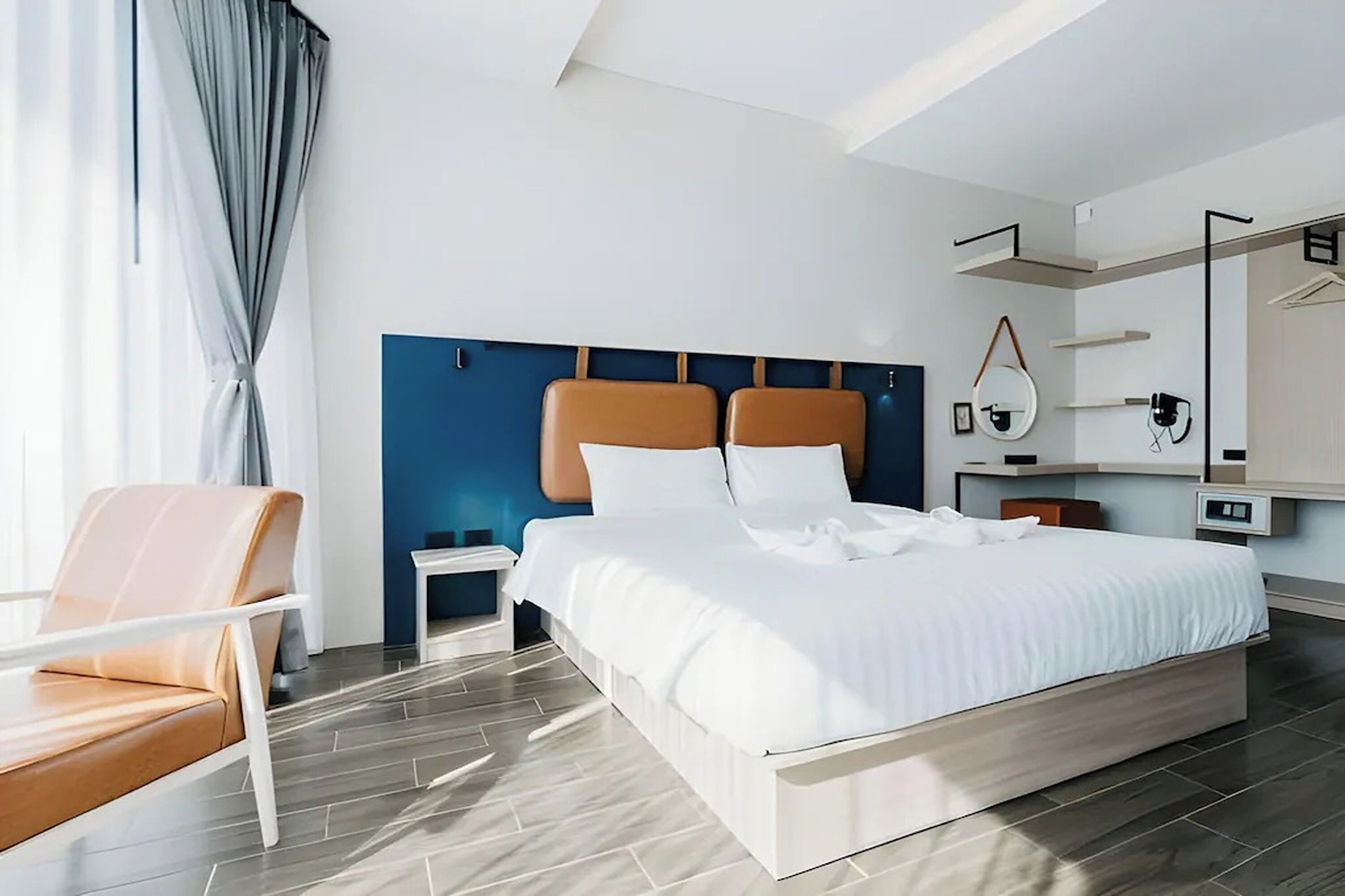 Quarto de hotel moderno com uma cama grande, mesa de cabeceira, uma cadeira e um guarda-roupa.