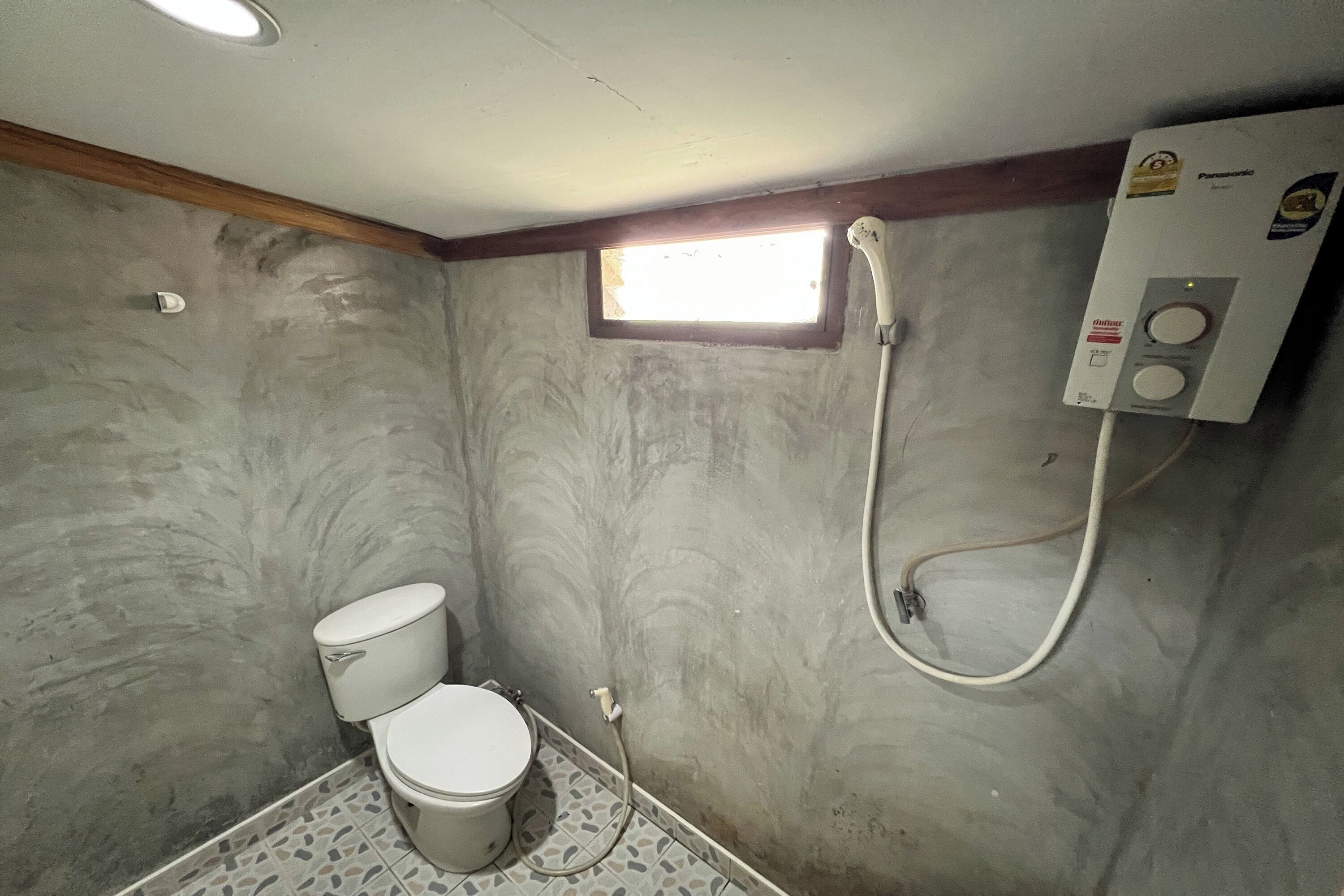 A small bathroom with a toilet, a shower, and a window.