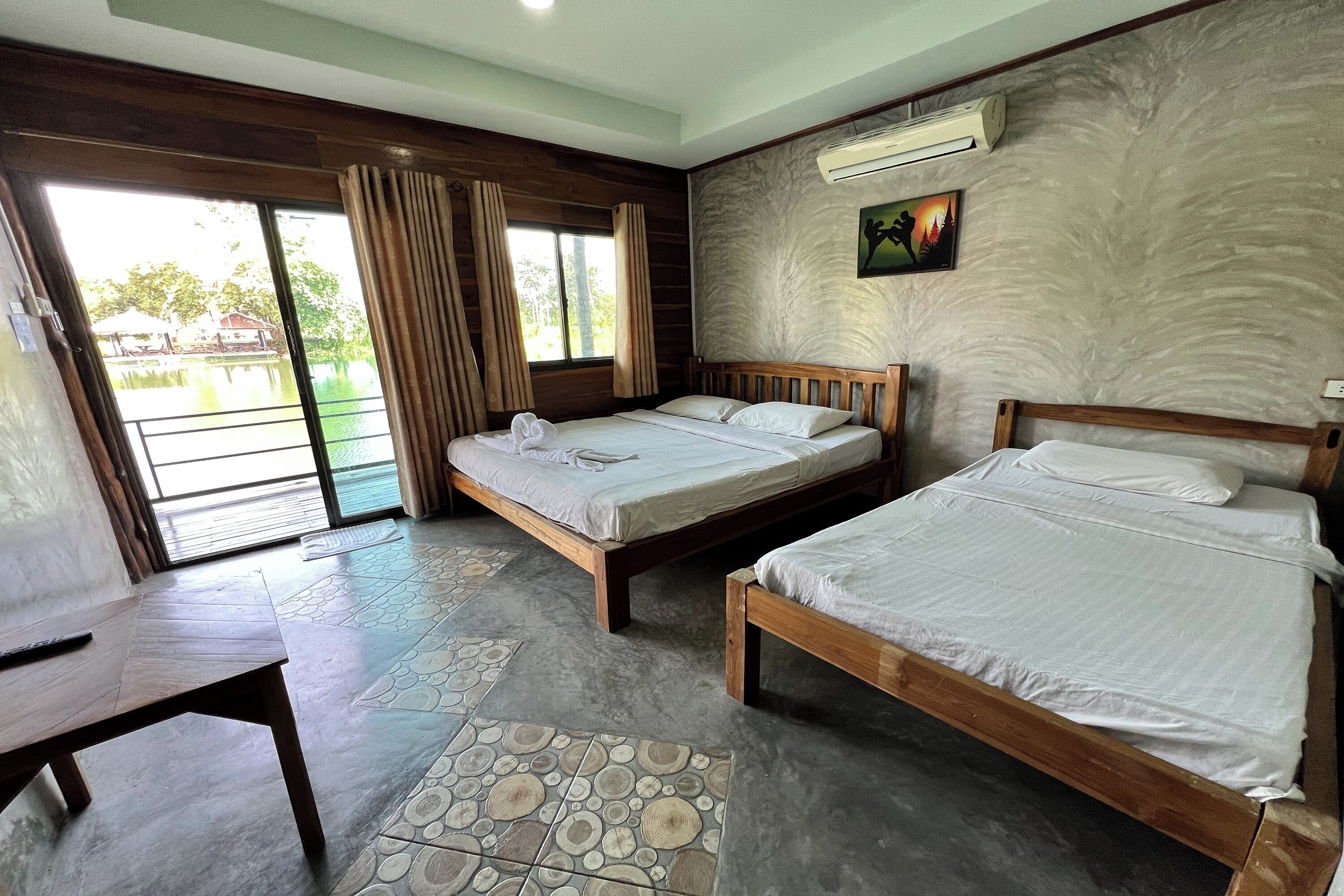 A hotel room with two wooden beds, a large window with curtains, a ceiling fan, and a view of a water body outside.