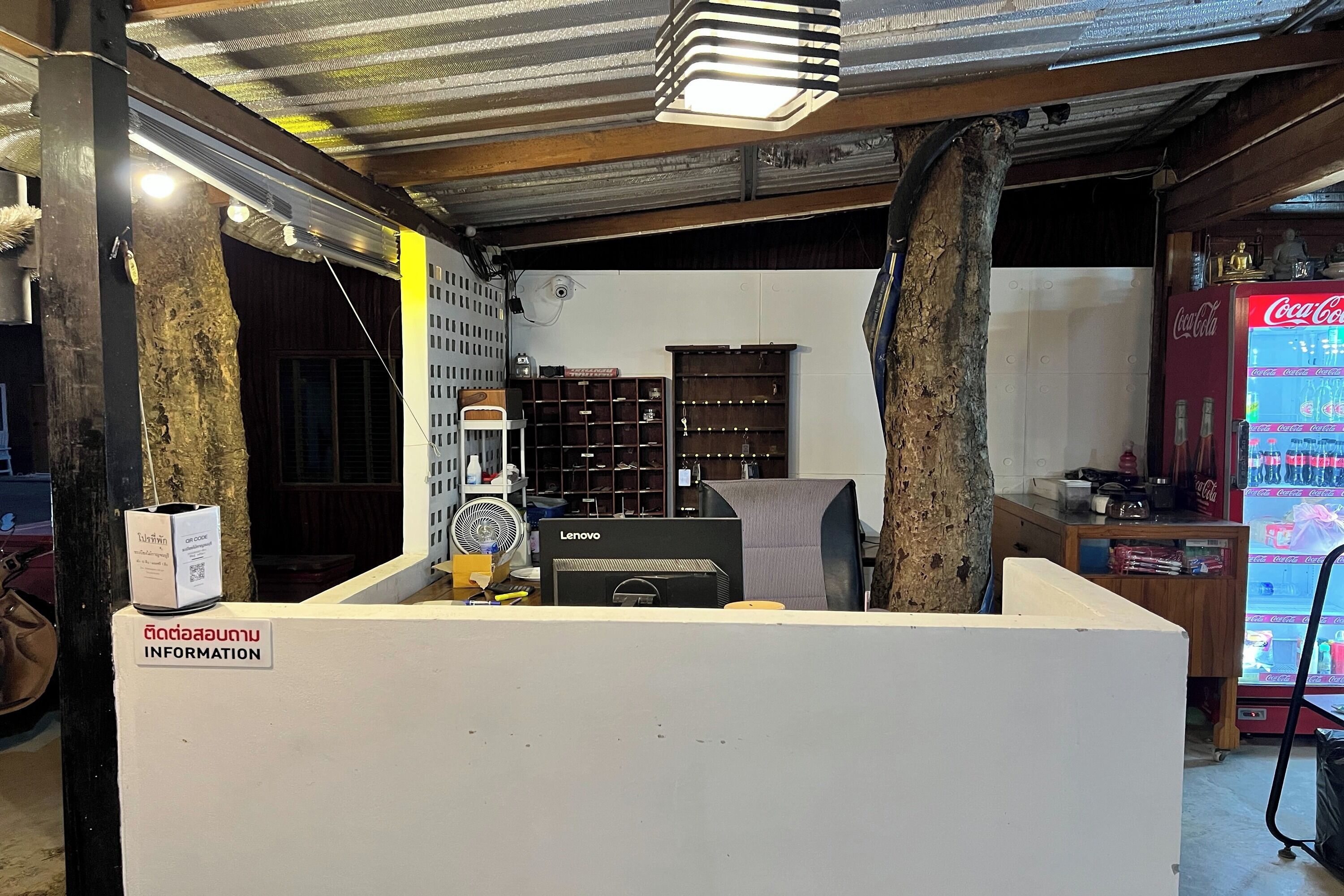 A reception area with a Coca-Cola refrigerator, a Lenovo computer, and a fan.