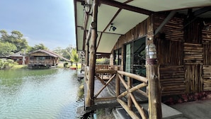 A wooden structure with a deck extending over water, featuring a railing and a covered area with a ceiling. - Rabiangmai Resort (Kanchanaburi)