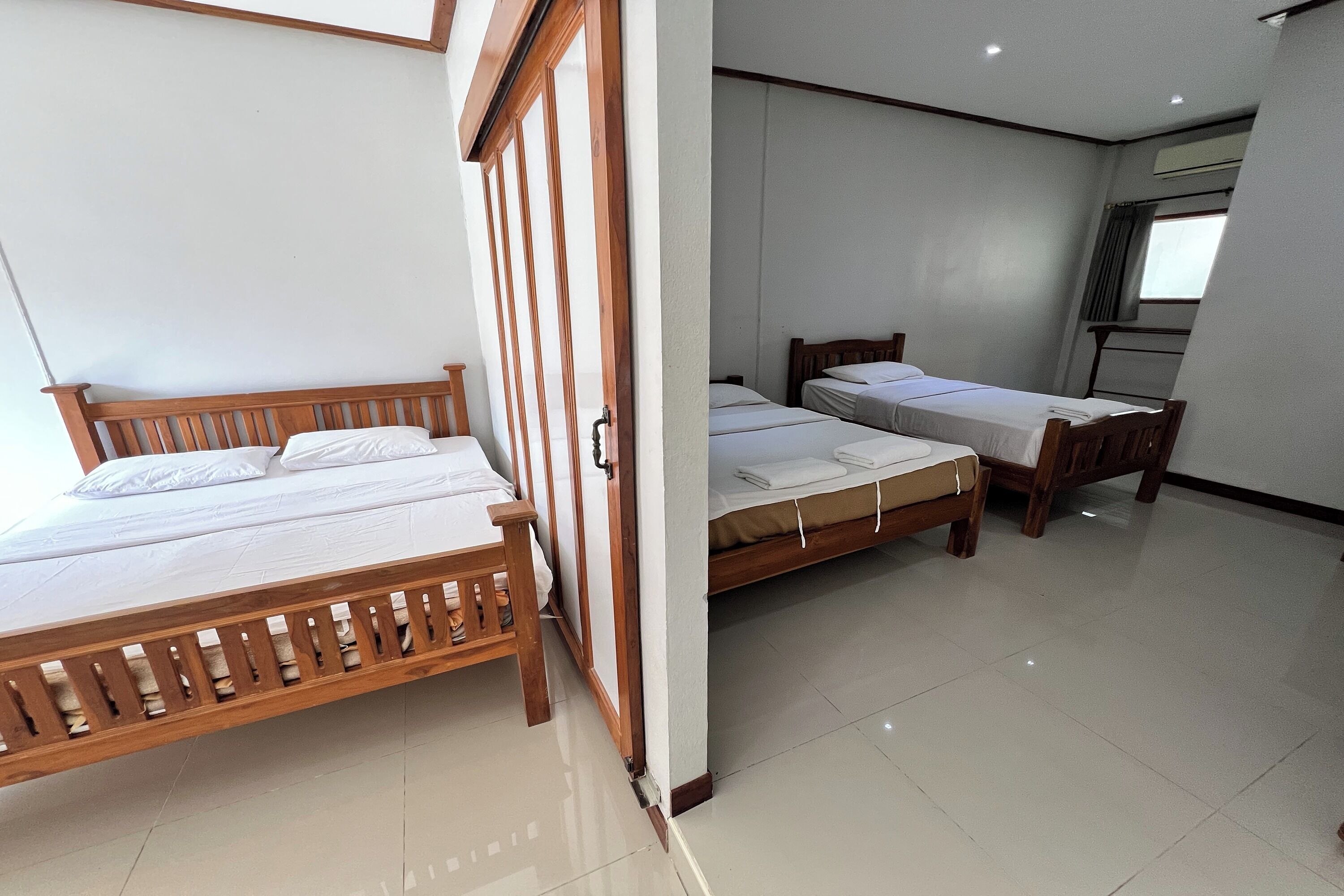 A hotel room with two wooden beds, a wooden wardrobe, and a tiled floor.