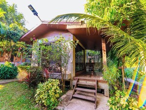 A covered outdoor area with a wooden staircase leading up to a porch, surrounded by lush greenery and plants. - Lion Cafe Resort (Hang Dong)