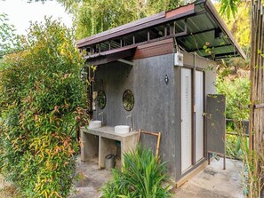 A small, enclosed outdoor bathroom with two sinks and a shower area, surrounded by greenery. - Lion Cafe Resort (Hang Dong)