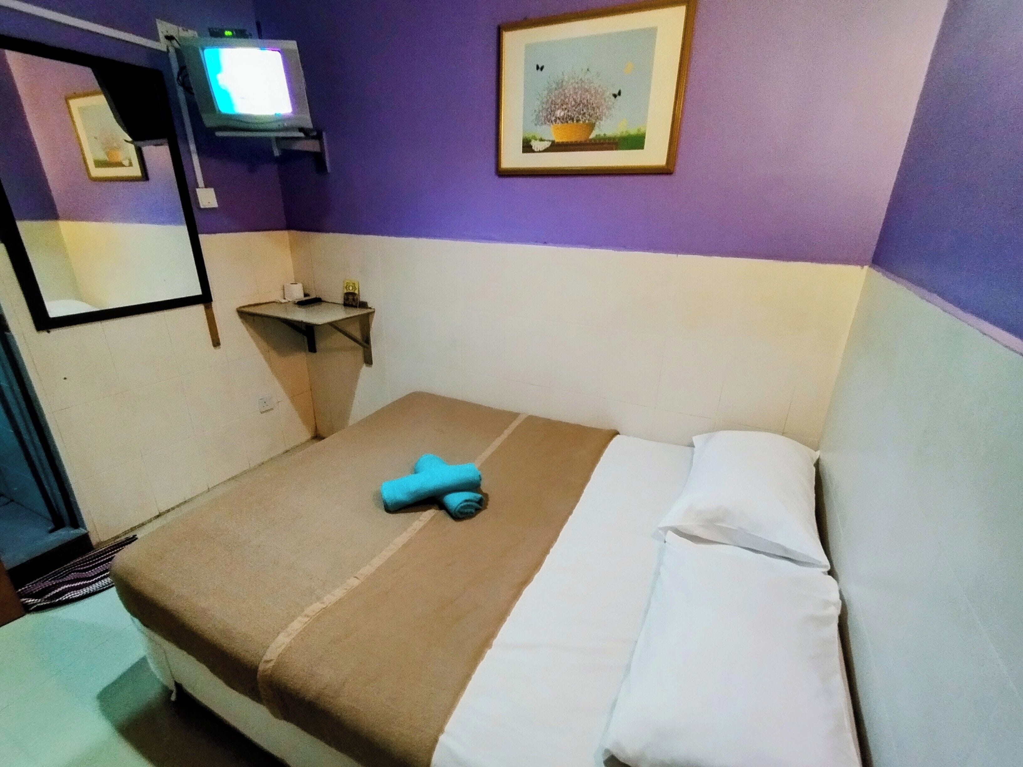 A room with a bed, a television mounted on the wall, a small shelf with toiletries, and a framed picture on the wall.