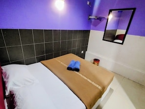 Ein Hotelzimmer mit Bett, einem kleinen Tisch, einem Spiegel und einer Wand in Lila und Weiß.