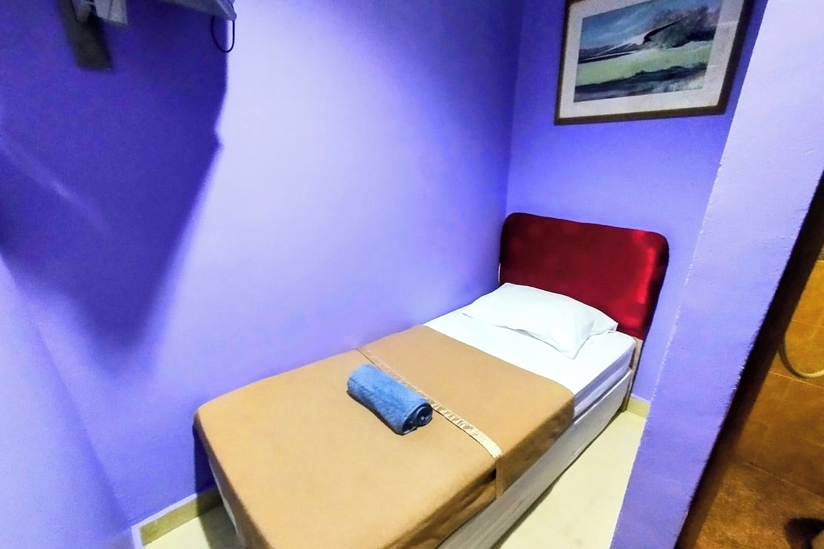 Ein Einzelbett mit rotem Kopfteil in einem Zimmer mit violetten Wänden.