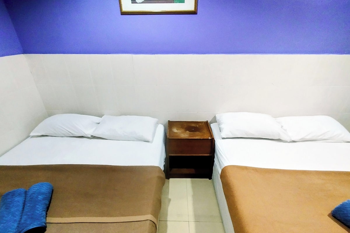 Ein Zimmer mit zwei Betten, jeweils mit brauner Bettdecke und weißen Kissen, und einem kleinen Nachttisch dazwischen.