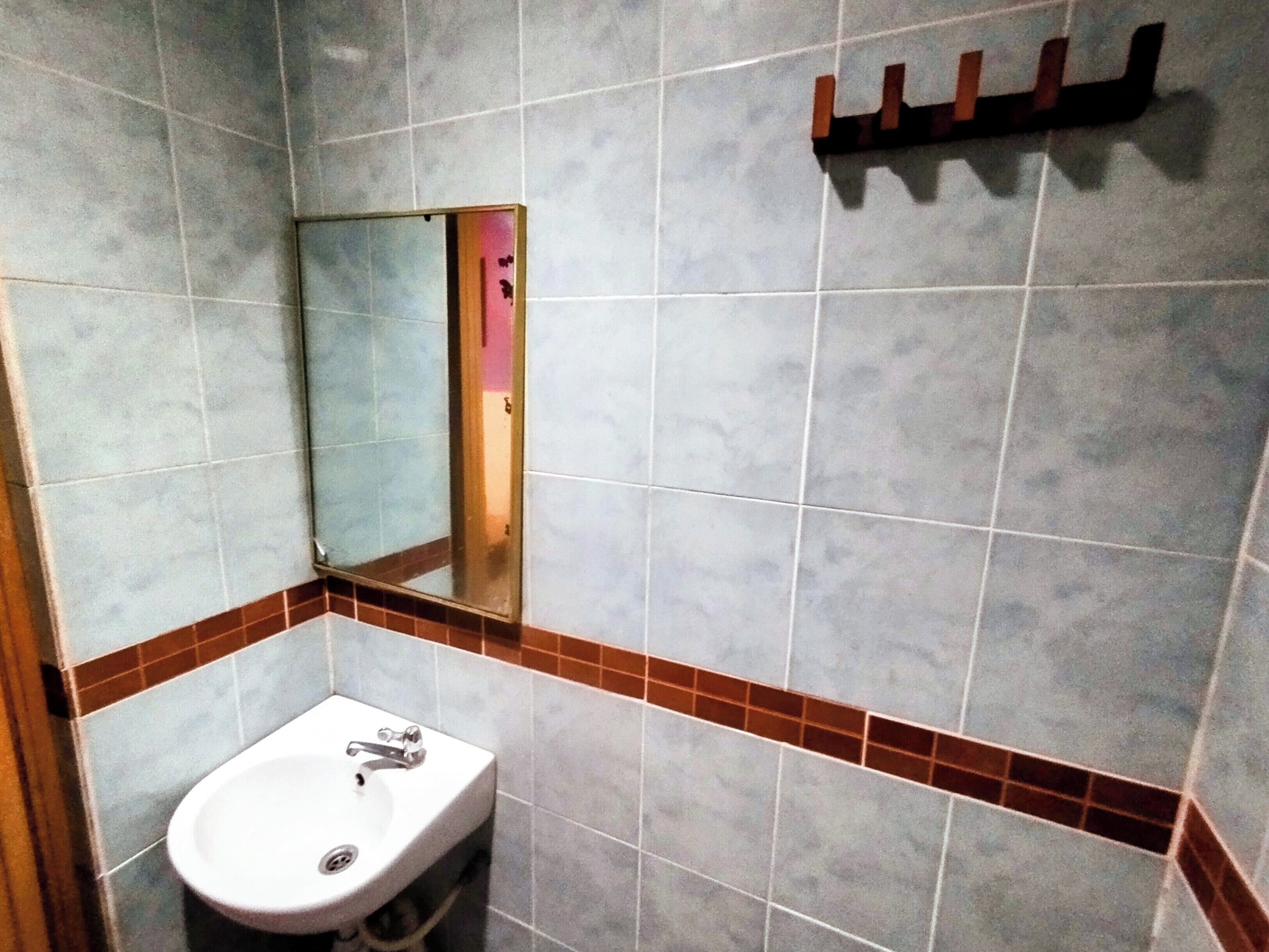 Un baño con lavamanos, espejo y paredes de azulejos.