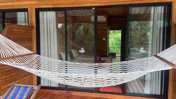 Uma cabana de madeira com rede, portas de vidro deslizantes e vista para o verde.