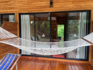 A wooden cabin with a hammock, sliding glass doors, and a view of greenery. - Mataburi River Kwai Resort (Sai Yok)