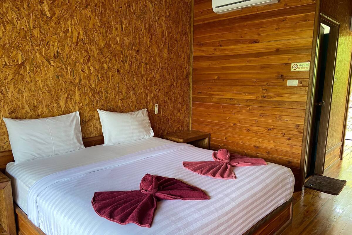Una habitación con paneles de madera, una cama, almohadas, un cartel de prohibición de fumar y una toalla sobre la cama.