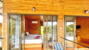 A wooden cabin with a balcony, a bed with white bedding, and a striped beach chair. - Mataburi River Kwai Resort (Sai Yok)