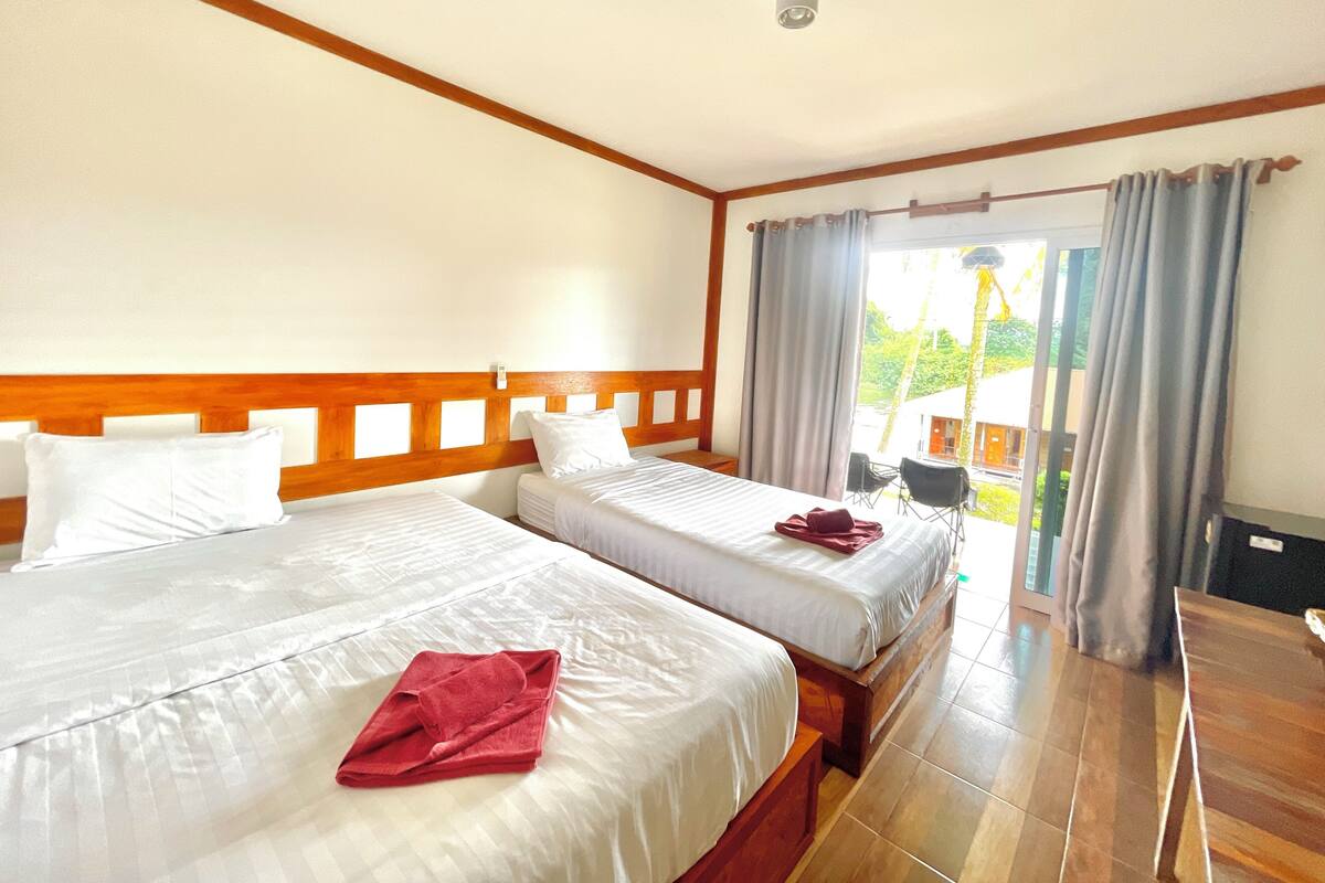 Habitación de hotel con dos camas, cabecera de madera, una mesita y vistas al exterior.