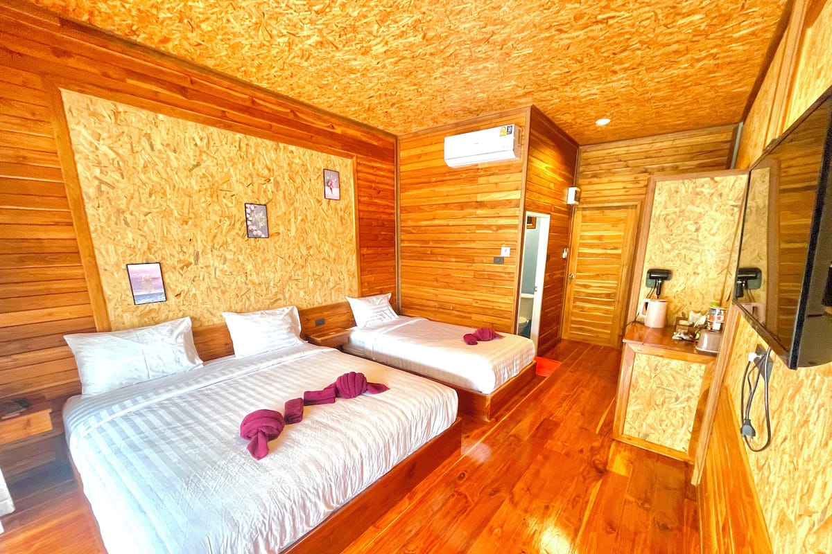 Una habitación con paneles de madera, dos camas, un espejo y una pequeña kitchenette.