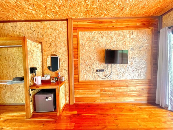 A room with wooden walls, a flat-screen TV mounted on the wall, a small refrigerator, a mirror, and a wooden bench. - Mataburi River Kwai Resort (Sai Yok)