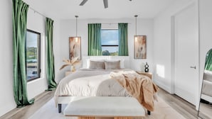 Een moderne slaapkamer met een bed, een bankje, een plafondventilator en kunst aan de muren.