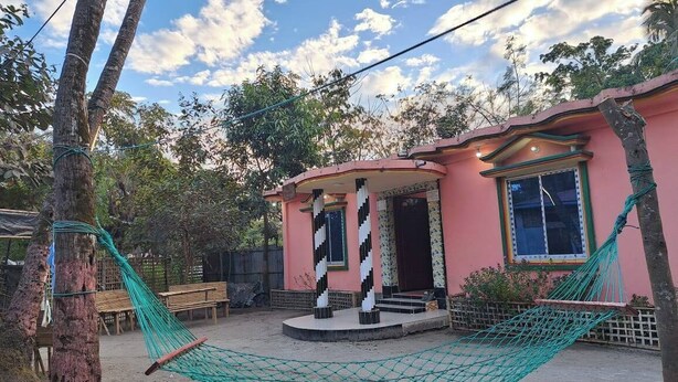 Um edifício rosa com varanda, rede e banco.