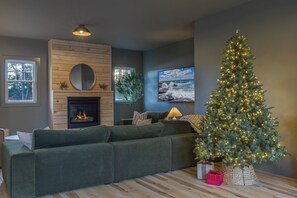 A cozy living room with a fireplace, a large Christmas tree, and a comfortable sofa.
