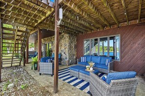 A covered outdoor seating area with wicker furniture, a stone wall, and a wooden ceiling. - 5K+ Sq Ft Waterfront Retreat; Sleeps 23–28+; Pool, Arcade, Beach, Kayak & More (Curran)
