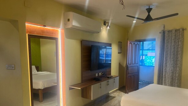 A hotel room with a bed, a TV, a wardrobe, and a mirror. - White Yellow Residency (Puducherry)