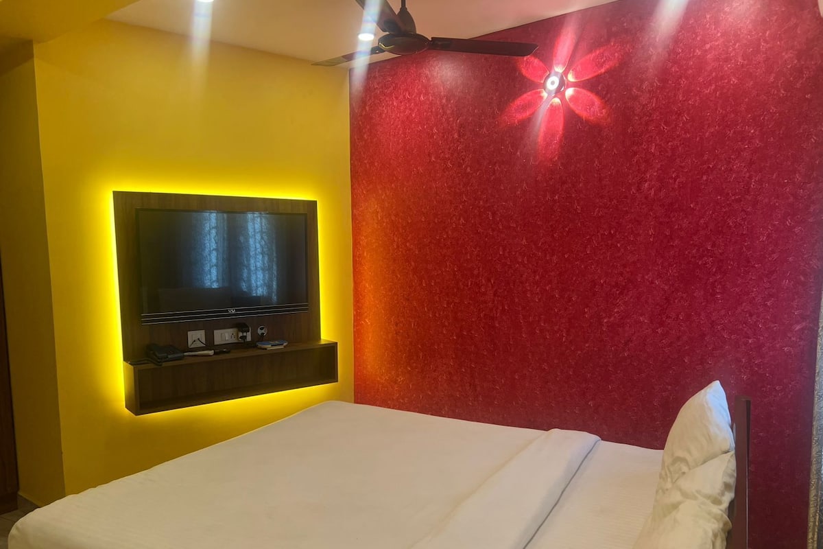 A hotel room with a bed, a mounted TV, and a ceiling fan.