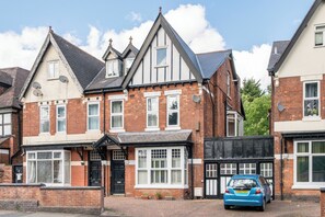 A two-story house with a brick facade, multiple windows, and a car parked in the driveway. - Apartment Sleeps 7 - Pets, Free Parking & WiFi (Birmingham)