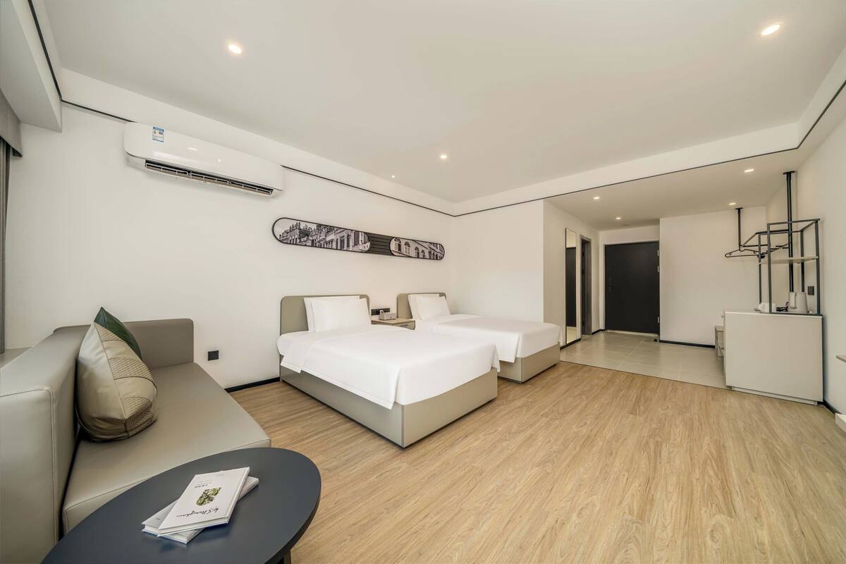 Ein modernes Hotelzimmer mit einer Couch, zwei Einzelbetten, einem kleinen Tisch und einer Klimaanlage.