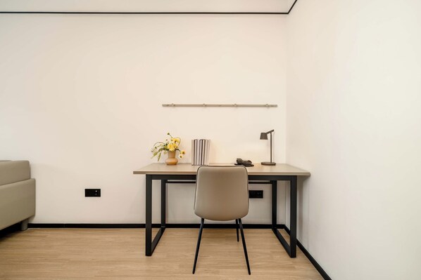 A minimalist office space with a desk, chair, and a vase of flowers.
