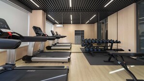 Ein Fitnessraum mit Laufbändern, Crosstrainern und einer Hantelbank.