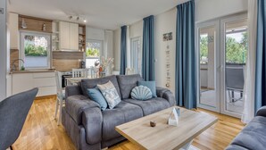 Uma sala de estar moderna com um sofá cinza, mesa de centro de madeira e uma área de jantar com mesa e cadeiras brancas.
