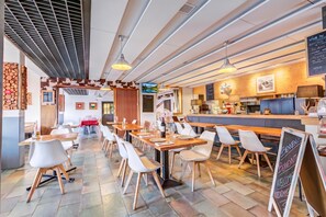 Interior moderno de restaurante con mesas y sillas de madera, una zona de bar y un panel con la carta.
