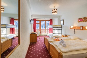 Een hotelkamer met stapelbedden, een bureau, een stoel, een televisie en een raam met uitzicht op met sneeuw bedekte bomen.