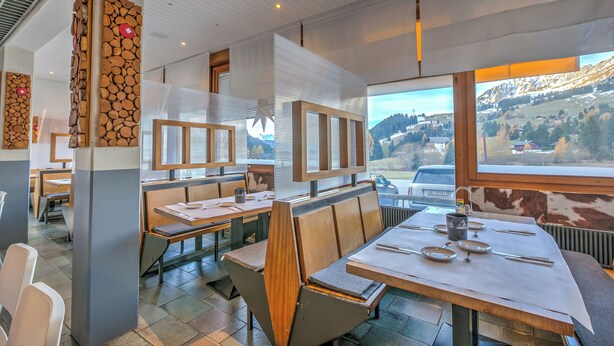 Un restaurante con bancos y mesas de madera, amplias ventanas con vista a la montaña y un diseño interior moderno.