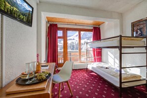 Una habitación con literas, un escritorio con una botella y vasos, una silla y una ventana con vistas a montañas.