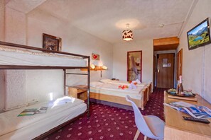 Habitación de hotel con literas, un escritorio con silla, televisión y baño visible a través de una puerta abierta.