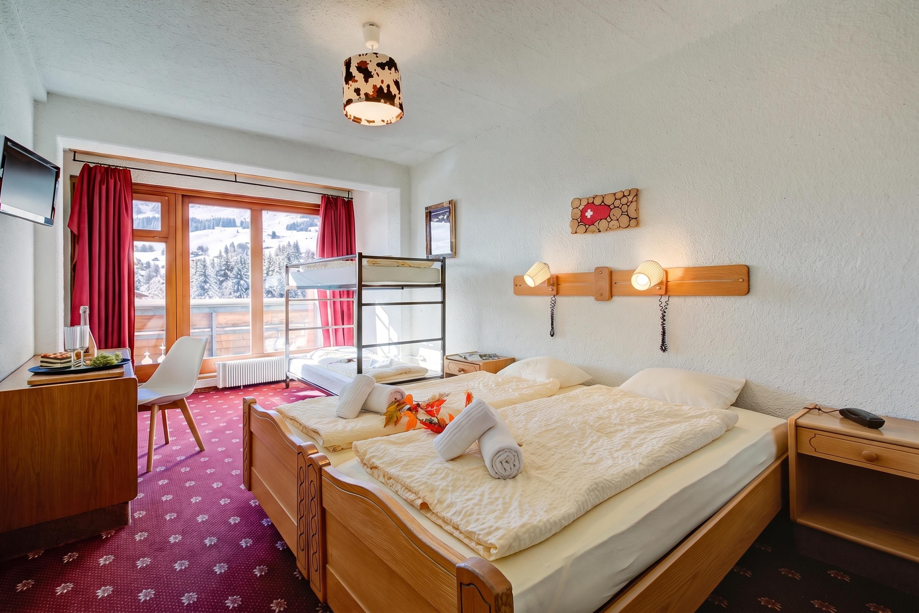 A hotel room with a bed, a desk, a chair, a TV, and a window with a view of a snowy landscape.
