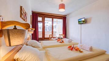 Ein Hotelzimmer mit zwei Betten, einem an der Wand befestigten Fernseher und einem Fenster mit Blick auf eine verschneite Landschaft.