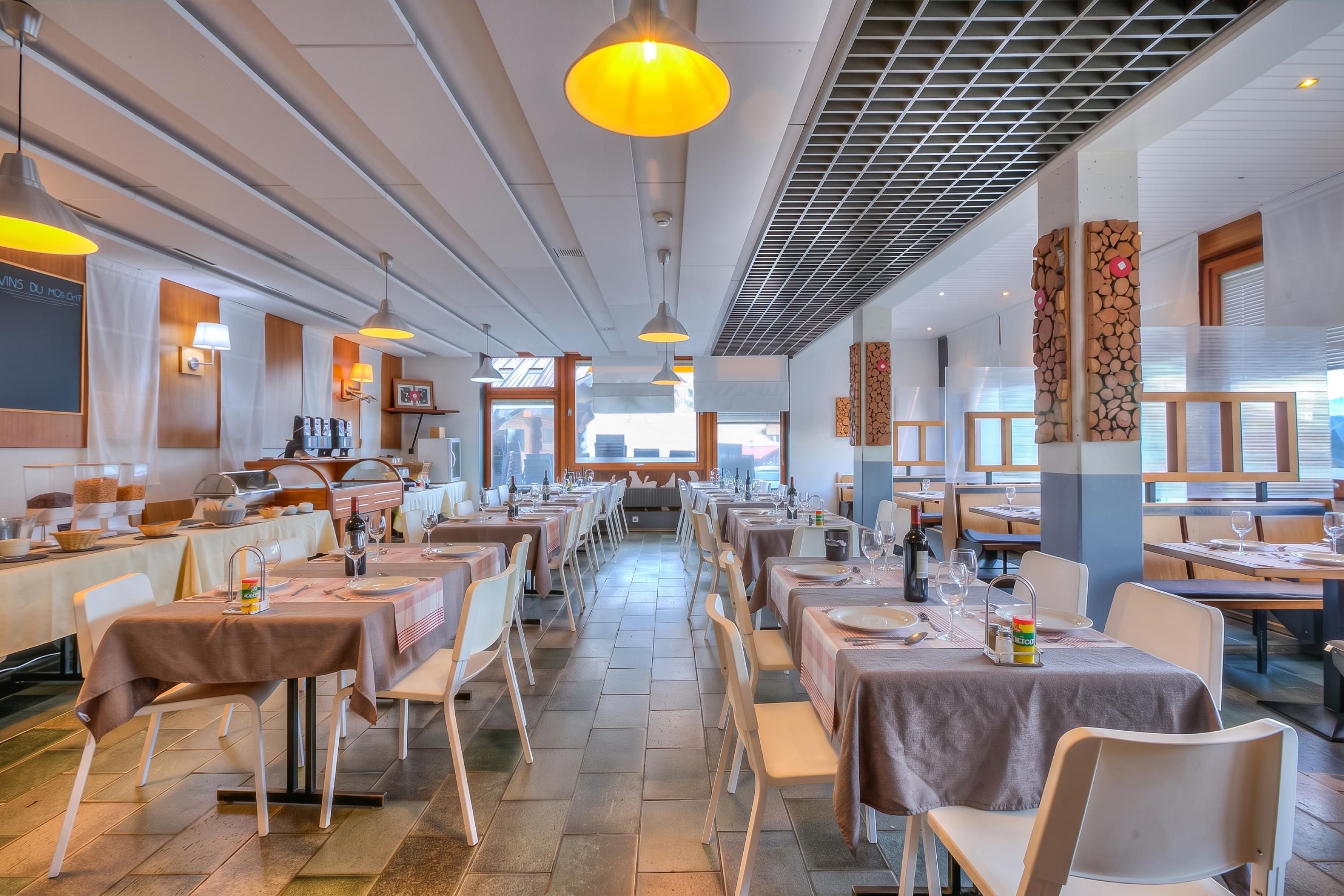 Un restaurant spacieux, doté de nombreuses tables et chaises, d’un éclairage au plafond et offrant une vue sur le paysage urbain grâce à de grandes fenêtres.