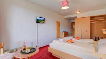 Ein Hotelzimmer mit einem Bett, einem kleinen Tisch mit Flasche und Gläsern, einem an der Wand montierten Fernseher und einem Holzschrank.