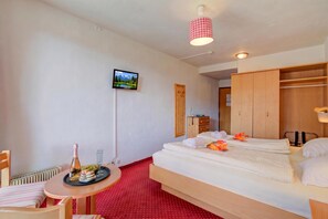 Hotelkamer met een bed, een kleine tafel met fles en glazen, een aan de muur bevestigde televisie en een houten garderobe.